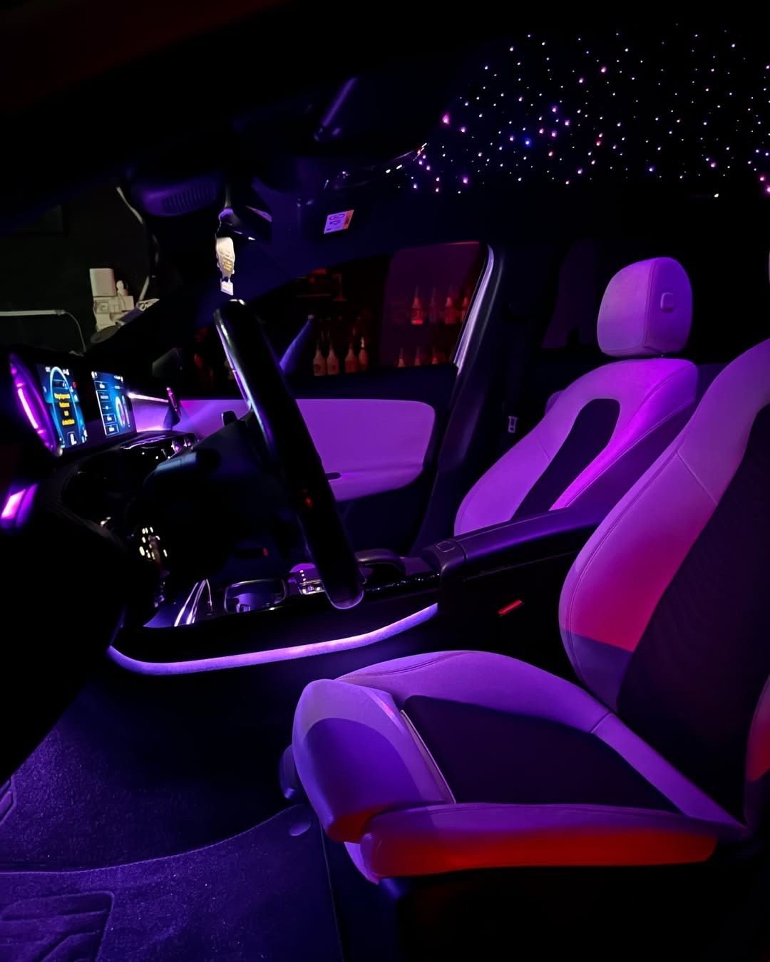 Interior of a car with ambient purple lighting, showcasing the dashboard, steering wheel, and seats.