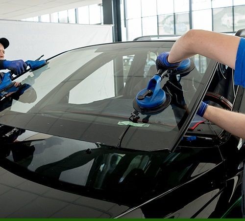 Technicians installing a windshield on a car using suction cups in an auto repair shop.