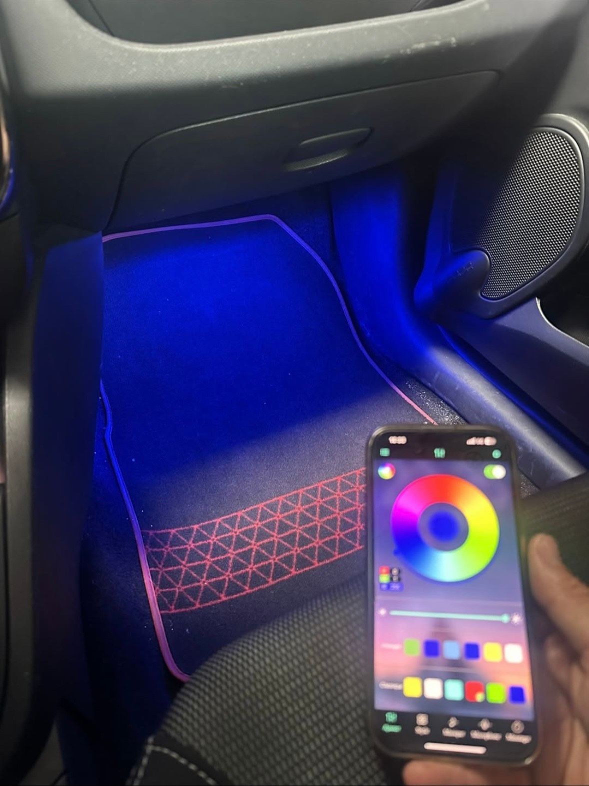 Car interior with blue floor lighting, phone displaying a color wheel for LED control.