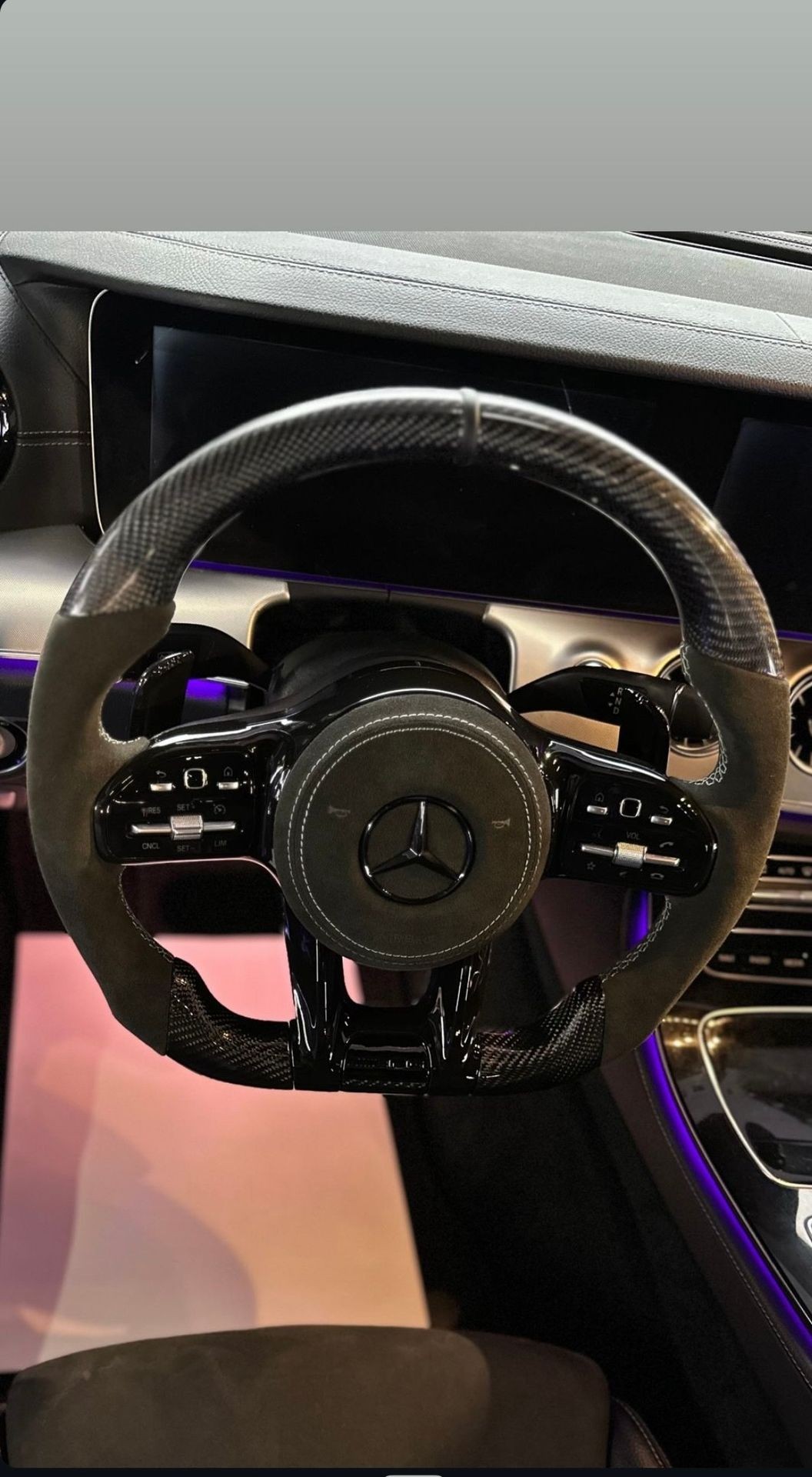 Luxury car interior featuring a sports steering wheel with carbon fiber and leather, ambient lighting in background.