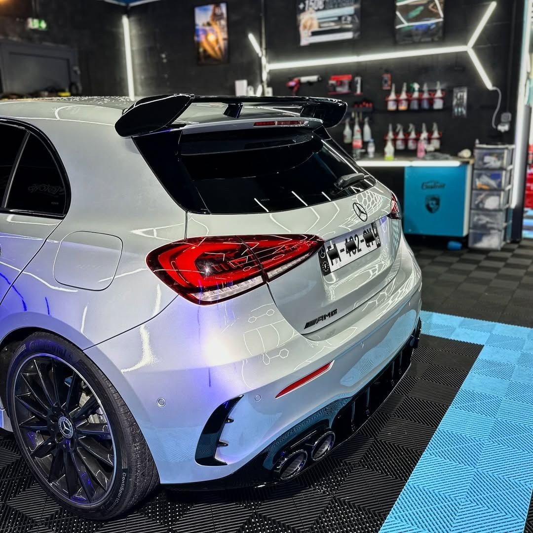 White sports car with rear spoiler and dual exhaust in a garage lined with car care products.