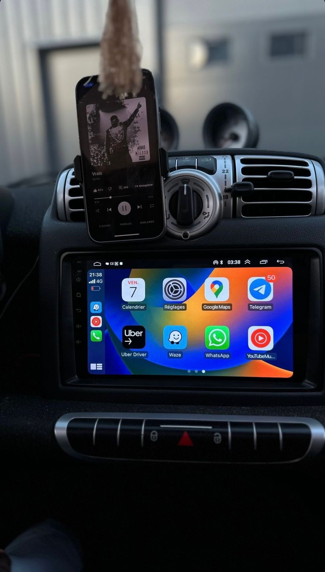 Car dashboard with smartphone playing music and navigation screen displaying various app icons.