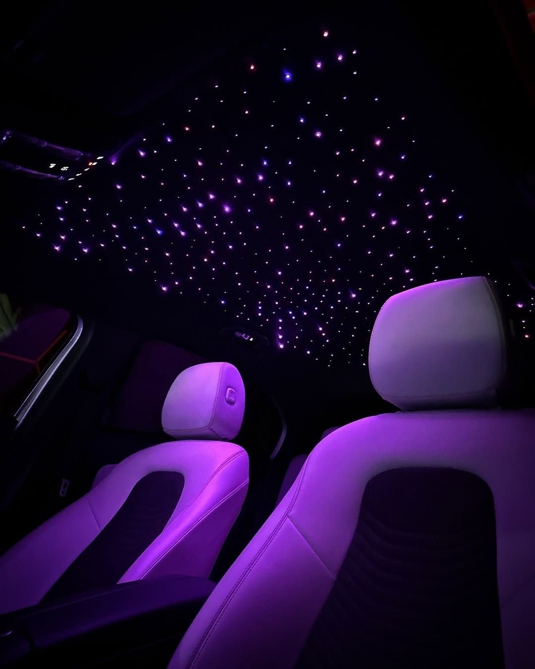 Interior of a car with starry ceiling lights and illuminated seats, creating a vibrant purple ambiance.